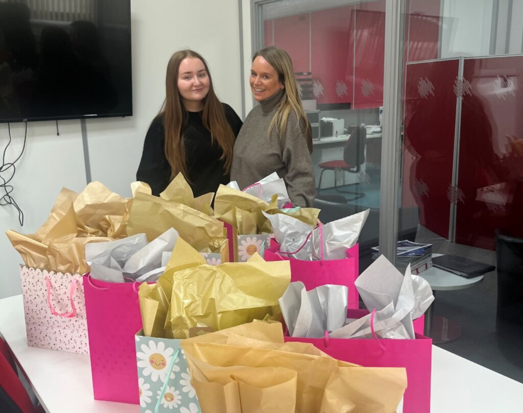 Administrator Lauren and HR Manager Carmel, standing behind several gift bags containing toiletries and Easter eggs.